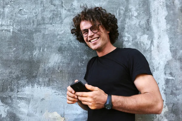 Sorrindo Homem Bonito Com Cabelo Encaracolado Segurando Telefone Celular Enquanto — Fotografia de Stock