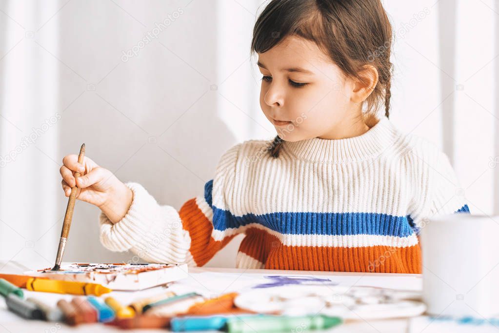 cute little girl drawing with brush at table 