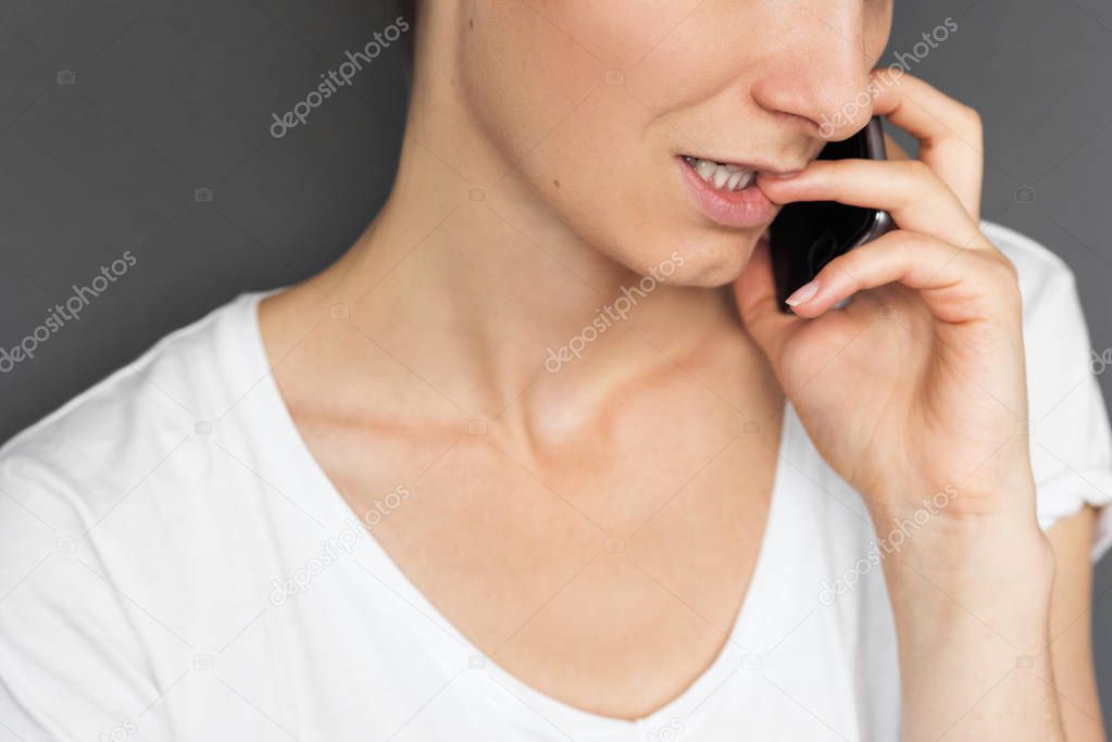 Cropped closeup portrait of beautiful female has phone conversation, uses modern cell phone, wears white T-shirt. People, lifestyle and technology concept.