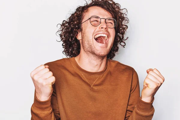 Retrato de estúdio de estudante ou homem de negócios bem sucedido feliz com cabelo encaracolado vestindo óculos redondos, gritando com expressão vencedora, punhos bombeados posando na parede branca. Pessoas, conceito de emoção — Fotografia de Stock