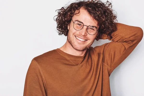 Horizontal front view portrait of handsome smiling young male with curly hair, wears round trendy spectacles, looking to the camera. Business man positn on white studio wall. Copyspace for advertising — Stock Photo, Image