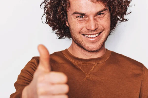 Closeup studio portrait of handsome man smiling with curly hair, posing for social advertisement with thumb up on white wall. Excited cheerful male student making good gesture. — Stock Photo, Image