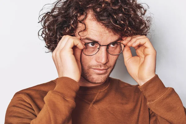 Horizontal closeup portrait of serious young male with curly hair, wears round trendy spectacles, looking to at one side. Business man posing on white studio wall. — Stock Photo, Image