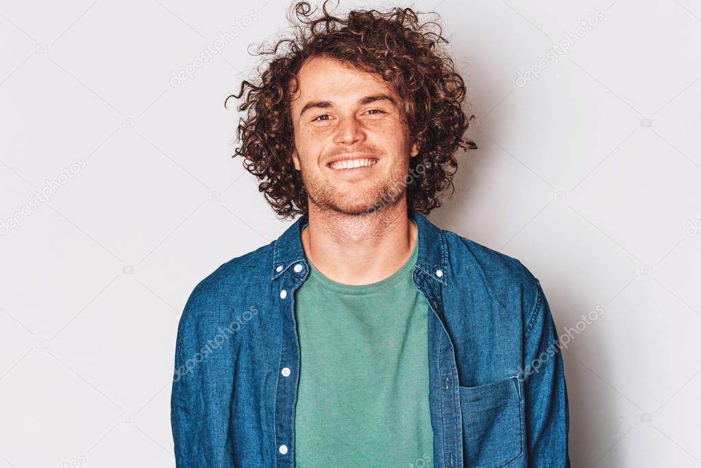 Handsome good-looking smiling male posing for advertisement wears denim shirt, isolated on white wall with copy space for your informational text. People and emotion concept