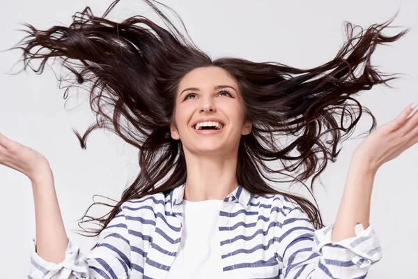 Estúdio retrato de bela mulher morena alegre com cabelo voador sorrindo e rindo olhando para cima com as mãos levantadas, posando sobre fundo branco . — Fotografia de Stock