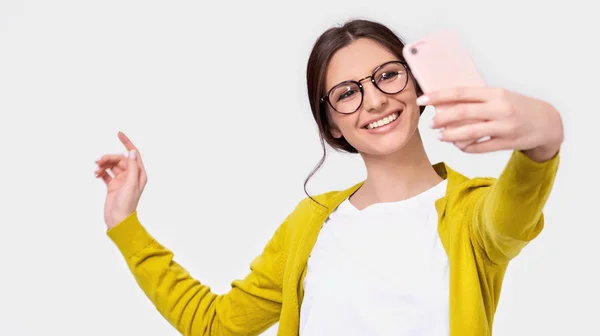 Bella giovane donna europea in abiti casual prendendo autoritratto sopra parete studio bianco. Felice femmina sorridente e prendendo un selfie sul suo smartphone, isolato su sfondo bianco . — Foto Stock
