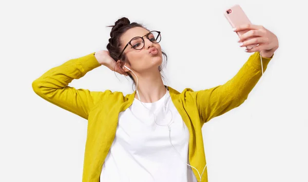 Indoor shot di una bella giovane donna europea in abiti casual invio bacio aria al suo ragazzo mentre in piedi e prendendo un selfie isolato su sfondo bianco studio . — Foto Stock