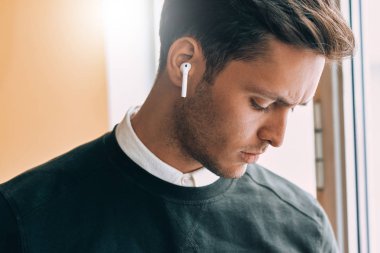 Portre portre üzgün genç yakışıklı adam kablosuz kulaklık kullanarak bir arkadaşıyla konuşuyor. Konuşma sırasında kablosuz kulaklık kullanarak ciddi Kafkas işadamı.