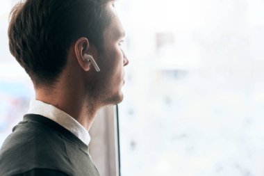 Yakışıklı delikanlı yatay görüntü bir arkadaş ve ofis, pencereden kablosuz kulaklık konuşmak seyir ile bir görüşmesi var. Beyaz işadamı kablosuz kulaklık kullanarak.