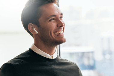 Portrait of happy young handsome man speaking with a friend telling good news using wireless earphones. Positive Caucasian businessman using wireless headphones during conversation. clipart
