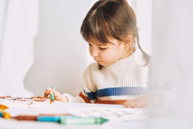 Güzel küçük bir kız portresi closeup petrol kalemler, evde beyaz masa başında oturan ile boyar. Çok okul öncesi çocuk gülümseyen ile renkli kalemler çizer. Kişi, çocukluk ve eğitim kavramı