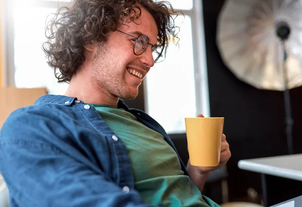 Вид збоку крупним планом портрет щасливого юнака фрілансера, який сидить в офісі, працюючи на ноутбуці. Усміхнений бізнесмен працює на портативному комп'ютері онлайн і п'є каву . — стокове фото