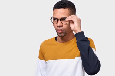 Giyen ve içine bakmak ciddi Afrikalı-Amerikalı gencin Studio yatay dikey yuvarlak trendy gözlükler. İş adamı beyaz stüdyo duvarda poz renkli kazak giyiyor. İnsanlar kavramı 