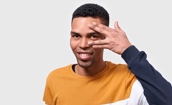 Beau jeune homme à la peau foncée cachant son visage avec la paume et montrant son oeil. Studio portrait de jeune homme couvrant son visage à la main et regardant la caméra tout en se tenant debout sur fond blanc — Photo