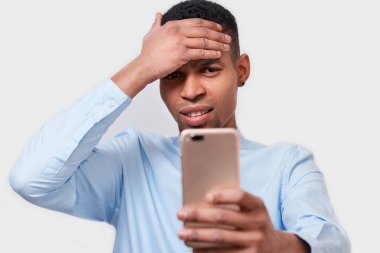 Genç Afrikalı-Amerikalı adam alır mesaj anımsatıcısını cep telefonu, mavi gömlek giymiş, beyaz stüdyo duvardan poz önemli toplantı hakkında unutuyor. Erkek online arkadaşlarınızla sohbet koyu derili