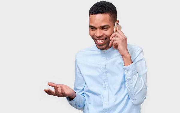 明るく、幸せな、白いスタジオ背景にポーズを探して、彼の友人に携帯電話で話している若いアフリカ系アメリカ人男性。ビジネスマンの同僚と彼のスマート フォンで話す. — ストック写真