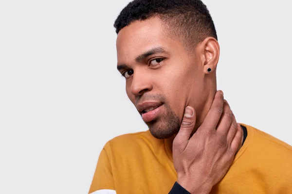 Detailní záběr mladého afroamerické muže dotýká jeho obličej a krk s rukou a při pohledu do kamery stoje proti bílé studio pozadí. Pohledný muž pocit čisté a svěží. — Stock fotografie