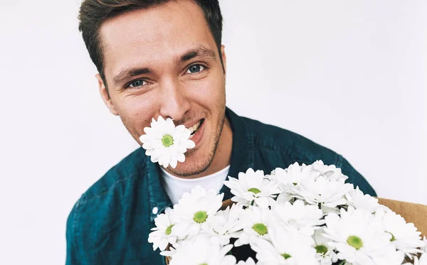 Homem bonito caucasiano feliz sorrindo com uma flor na boca e buquê de flores brancas. Homem atraente com um monte de flores se preparando para um encontro com sua namorada. Dia dos Namorados. Dia das Mães — Fotografia de Stock