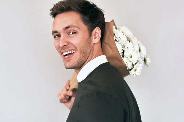 Knappe jongeman glimlachend en het leveren van een boeket van witte bloemen. Aantrekkelijk mannelijk model met een bos van bloemen die voorbereiden op een datum met vriendin. Aftelkalender voor Valentijnsdag. Mother's Day concept — Stockfoto