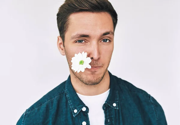 Zbliżenie Portret mężczyzny atrakcyjnego, uśmiechając się z kwiatem w ustach pozowanie na białej ścianie. Atrakcyjny model mężczyzna z biały kwiat z balnk speca kopiowania tekstu promocyjnego. Dzień matki. — Zdjęcie stockowe