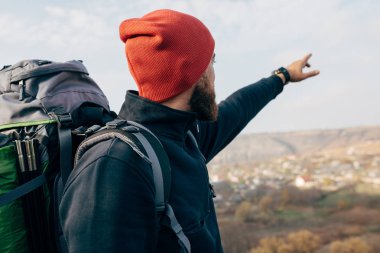 Arka görünüm görüntüsü genç fiyatı kırmızı şapkalı erkek ufuk için bir şeyler gösteriyor dağlarda, hiking. Gezgin sakallı adam dağcılık sonra rahatlatıcı. Seyahat, insanlar ve yaşam tarzı kavramı