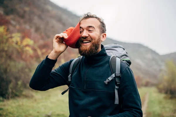 Outdoor portrait of happy hiker young man with red hat, hiking in mountains. Traveler bearded male smiling and feel happy after trekking during vacation. Travel, people and lifestyle concept