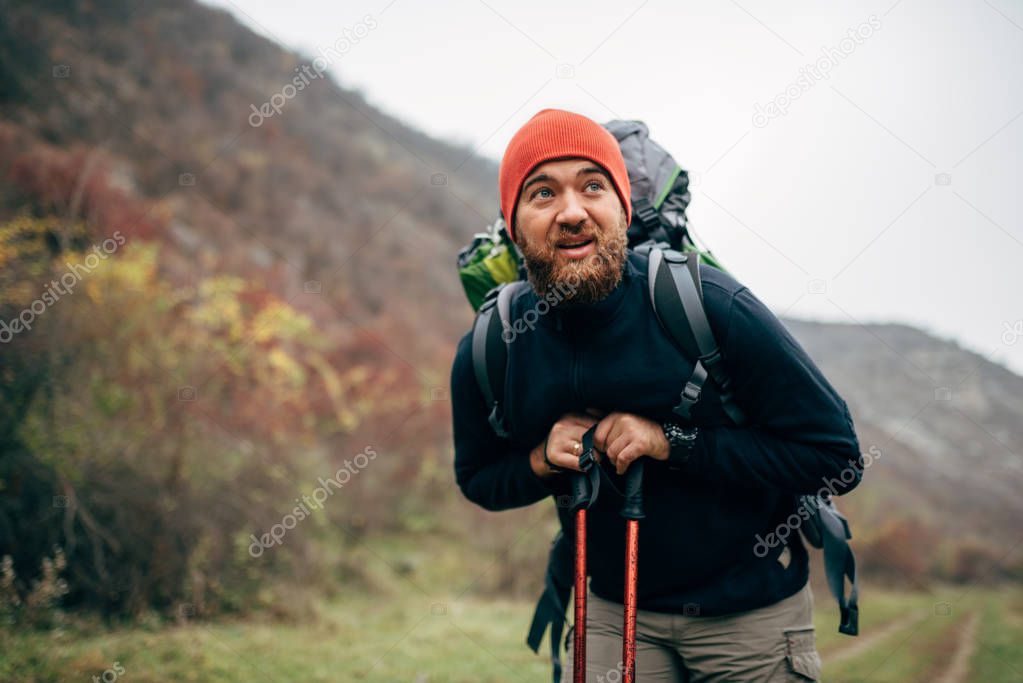 Outdoor shot of handsome Caucasian hiker young man hiking in mountains with travel backpack. Traveler bearded male have a break after trekking during vacation. Travel, people and lifestyle concept