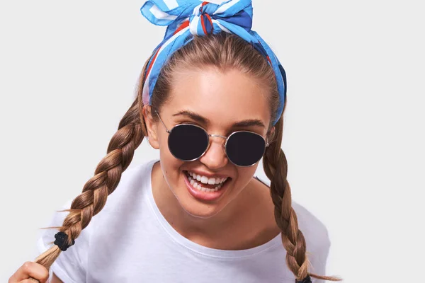 Close up portrait of young pretty woman wearing white t-shirt, blue headband and sunglasses with braids hairstyle, isolated on white background — Stock Photo, Image