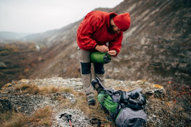 Outdoors shot of traveler bearded man preparing tent camping gear in mountain. Young male explorer hiking in mountain. Travel, lifestyle and journey concept. Active rest and mountain climbing. 