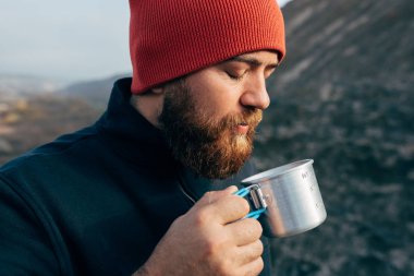 Açık havada sıcak içecek içme dağlarda trekking sonra rahatlatıcı bir adam portresi kapatın. Bir fincan çay sonra yürüyüş tutarak Gezgin erkek kırmızı şapkalı. Seyahat, insanlar, spor ve yaşam tarzı