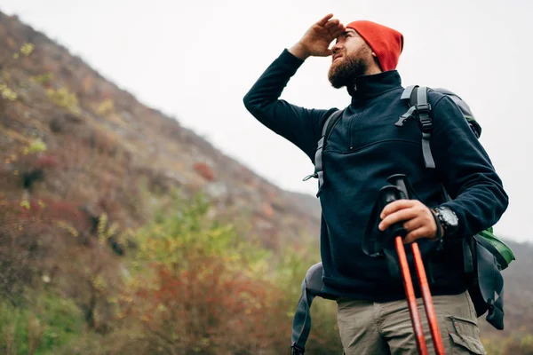 Outdoor horizontal shot of handsome hiker young man hiking in mountains with travel backpack. Traveler bearded male have a break after trekking during vacation, looks away. Travel, people, lifestyle