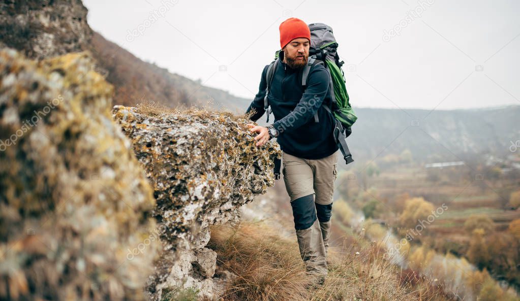 Bearded young male hiking in mountains with travel backpack. Traveler man trekking during his journey. Travel, people, healthy lifestyle concept
