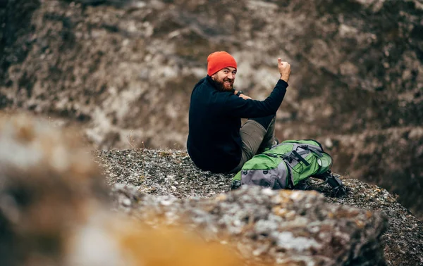 Bild eines jungen Mannes, der sich nach einer Wanderung in den Bergen entspannt. Rückansicht eines Reisenden mit rotem Hut, der allein sitzend nach dem Bergsteigen eine Pause einlegt. Reise- und Lifestylekonzept — Stockfoto