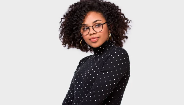 Imagem de estúdio da jovem afro-americana bonita, usa roupas casuais e óculos. Afro fêmea de blusa preta posando sobre a parede branca. Conceito de pessoas e emoções — Fotografia de Stock