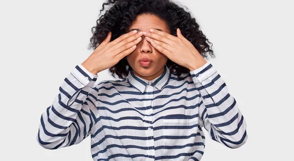 Joven afro-americana de buen aspecto con camisa a rayas, cubriendo los ojos con palmas y haciendo un beso de aire, esperando ser besada. Juguetona hembra de piel oscura jugando a las escondidas, busca y mira un boo . — Foto de Stock