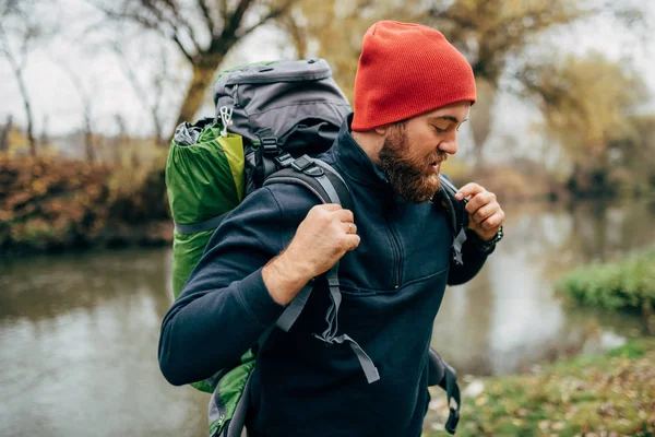 Yan görünümü çekim genç fiyatı ile dağlarda hiking erkek sırt çantası seyahat. Gezgin bir nehir yakınında dağcılık ayakta sonra adam rahatlatıcı sakallı. Seyahat, insanlar ve sağlıklı yaşam konsepti — Stok fotoğraf