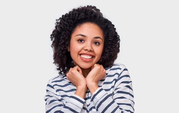 La joven afroamericana bastante feliz con una sonrisa positiva, cogida de la mano en la barbilla, mirando a la cámara, tiene una expresión alegre. Encantadora hembra de piel oscura tiene emociones positivas . —  Fotos de Stock