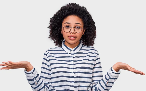 Intrigado muito afro-americano jovem mulher ombros de ombros, parece incerto, confundido com palmas das mãos abertas, tem dúvidas. Uma mulher de pele escura não pode fazer escolhas. Pessoas emoções e sentimentos conceito . — Fotografia de Stock