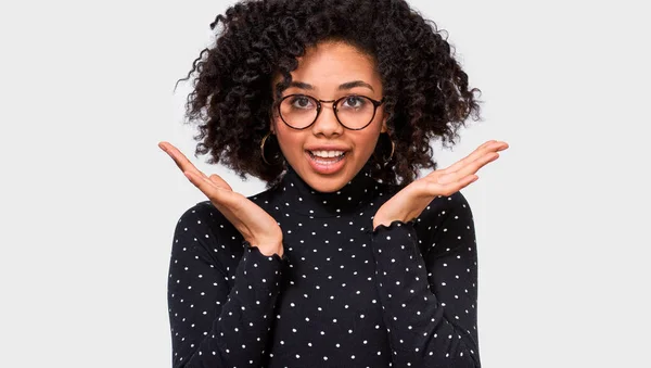 Sorprendido Afro joven mujer tiene expresión asombrada. Hermosa mujer oye algo increíble, mantiene las manos abiertas, aislado sobre fondo blanco con espacio de copia para su contenido promocional. Emociones — Foto de Stock