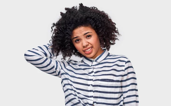 Estudante jovem afro-americana incerta tem expressão de dilema, franze a cara e olhe para a câmera. Mulher de pele escura duvidosa não pode fazer escolha, isolado na parede do estúdio branco — Fotografia de Stock