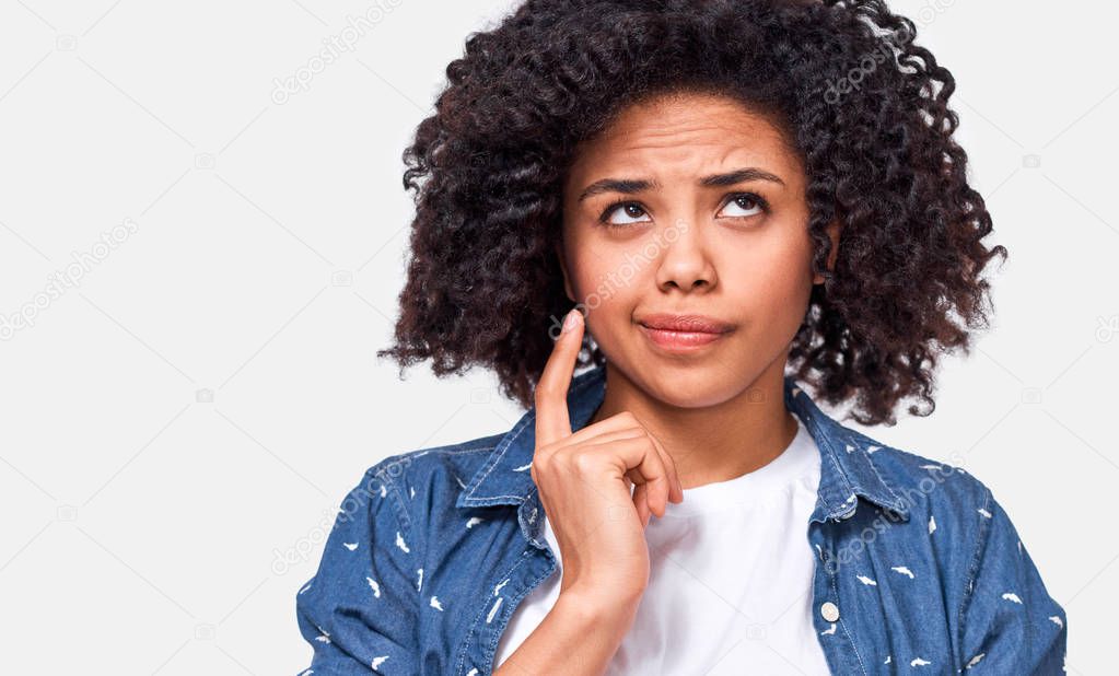Close up shot of uncertain African American woman has puzzled expression, frowns her face and looking up. Doubtful dark skinned female can t make choice, has questioned expression, isolated on white. 