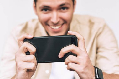 Çekici beyaz genç gülümseyen ve çekici fotoğraf onun cellphone tarafından beyaz stüdyo duvar karşı rahat forması giyen adam. Akıllı telefon üzerinden olumlu erkek blogging. İnsanlar, yaşam tarzı, teknoloji kavramı