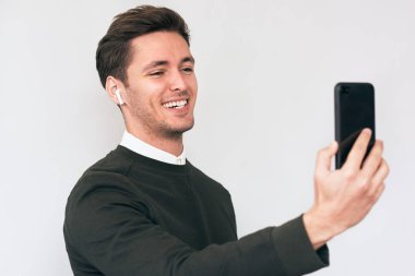 Gülümseyerek mutlu bir adam ve beyaz stüdyo arka planda, cep telefonu ekranına bakarak ve kendi kendine portre konuşuyor, web sayfalarını tarama ve güzel arkadaşları ile sohbet ederken gülümseyen izole ayakta.