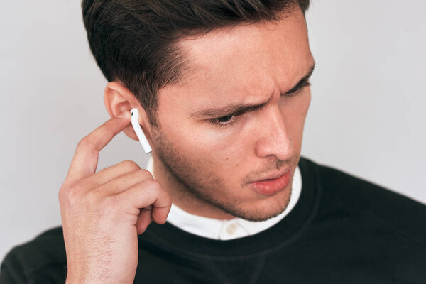 Closeup studio portrait of sad young Caucasian handsome man speaking with a friend using wireless earphones. Serious businessman using wireless earbuds during conversation. People, technology concept