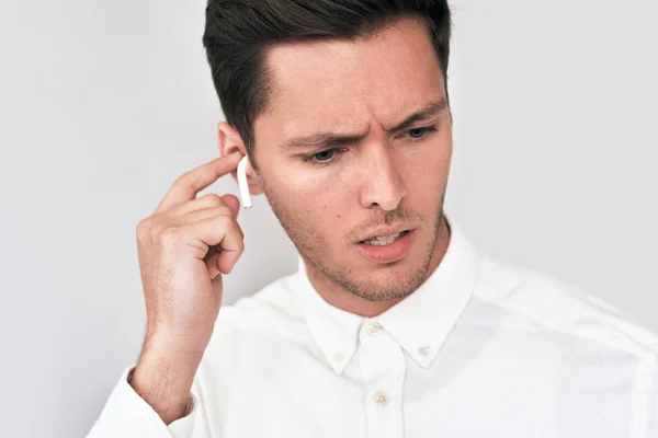 Closeup portrait of sad young handsome man wearing white shirt and speaking with a friend using wireless earphones. Serious businessman using wireless earbuds during conversation. People, technology — Stock Photo, Image