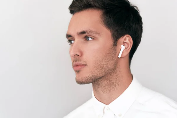 Серйозні гарний юнак позують з бездротові навушники, на тлі білої студії. Вид збоку постріл кавказьких бізнесмена за допомогою безпроводових навушників. Люди, технології та бізнес-концепції — стокове фото