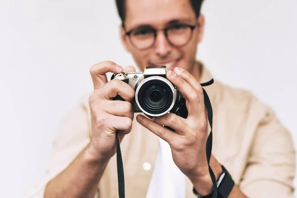 Immagine di giovane uomo sorridente e scattare foto sulla macchina fotografica digitale, in posa su sfondo bianco studio. Giovane maschio indossa abbigliamento casual e occhiali alla moda, blogging e guardando al display della fotocamera . — Foto Stock