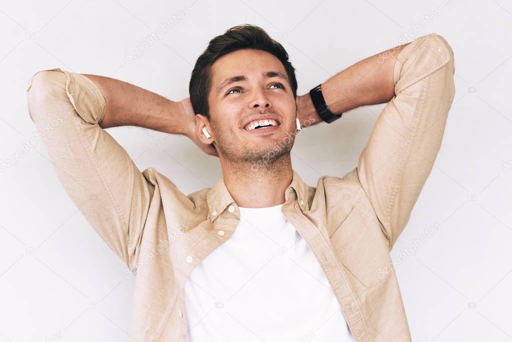 Relaxed handsome young man wearing casual outfit, holding hands behind head enjoying his free time, isolated on white studio background. People, lifestyle and emotions concept