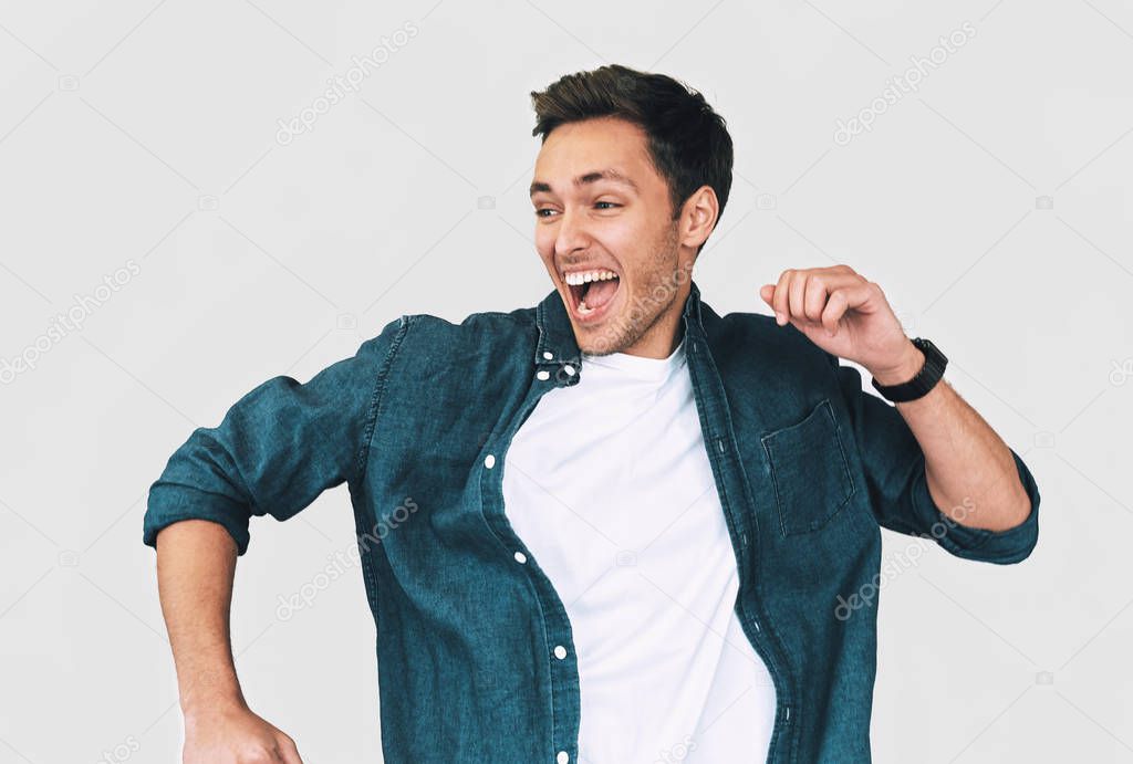 Cheerful, funny man wearing denim shirt and white t-shirt, jumping with raised arms, celebrating victory, having fun, isolated on white background. Happy student male rejoices triump. People emotions