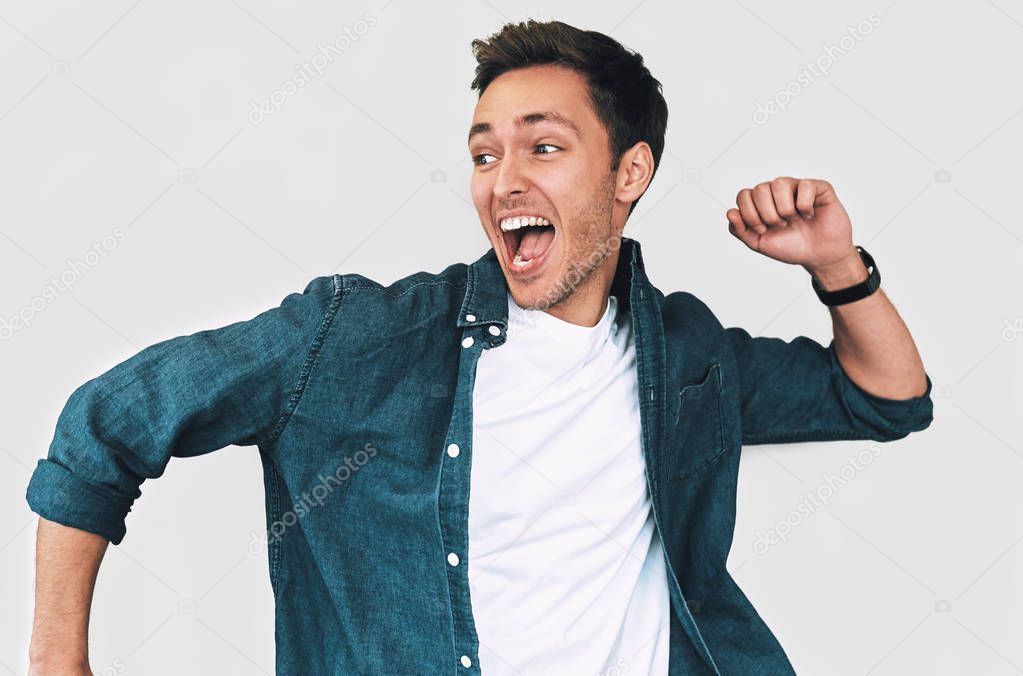 Studio portrait of flying cheerful, funny and happy man wearing denim shirt and white t-shirt, jumping with raised arms, celebrating victory, having fun, isolated on white background. Positive people